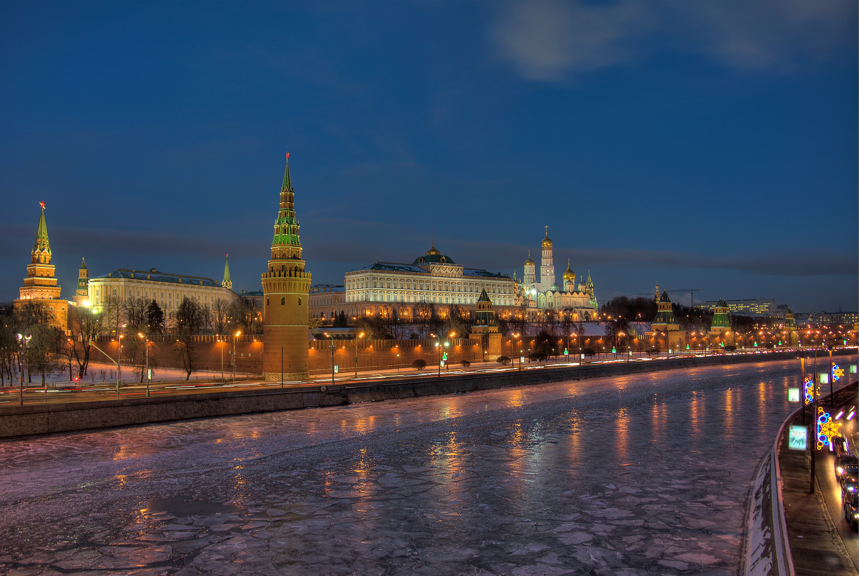 El Kremlin de Moscú de noche, visto desde el otro lado del río Moscova congelado, con las torres de la muralla y el Gran Palacio del Kremlin iluminados.