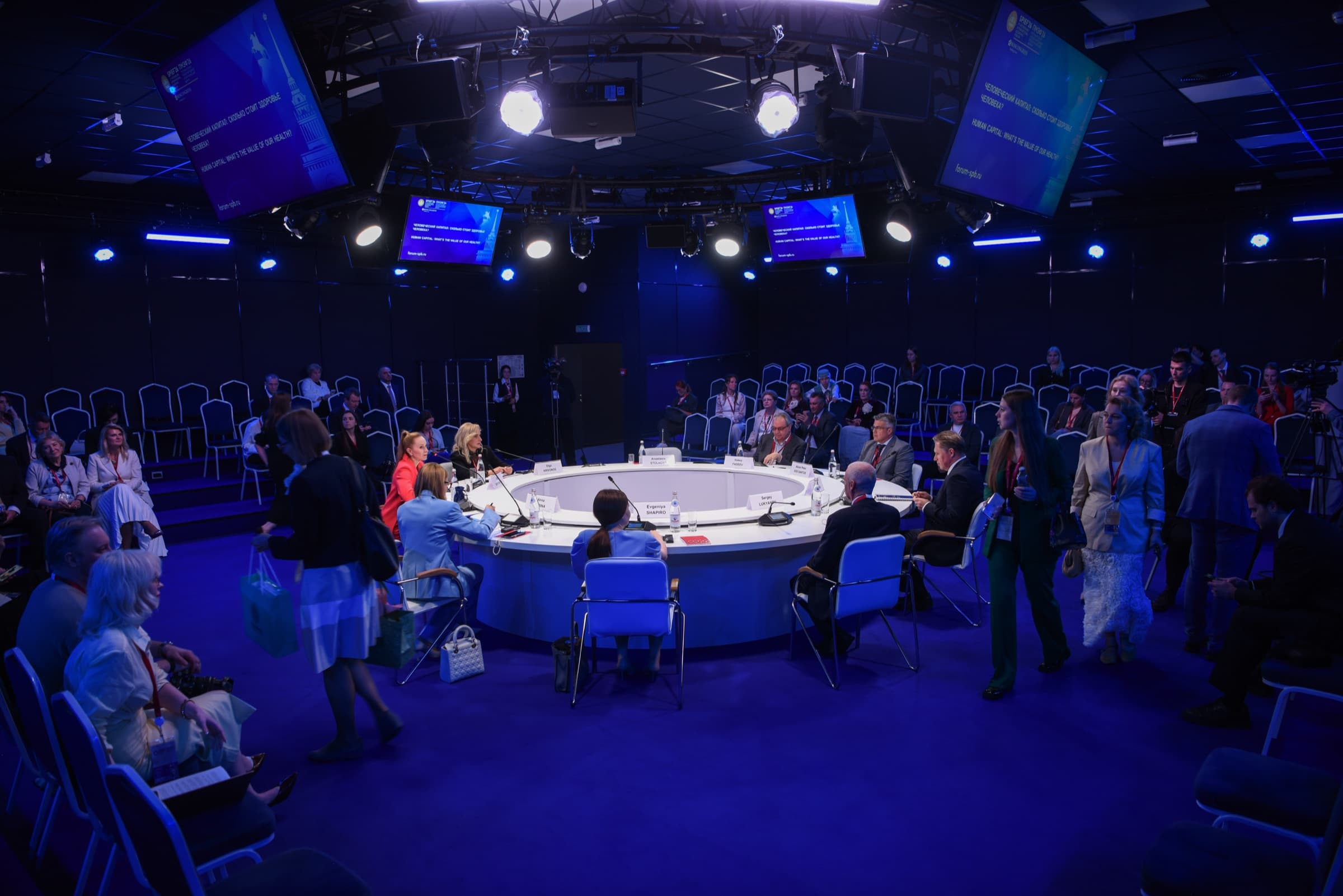 Mesa redonda del SPIEF 2026 vista desde arriba, con participantes sentados alrededor de una mesa circular blanca y pantallas que muestran el título de la sesión sobre capital humano y salud.