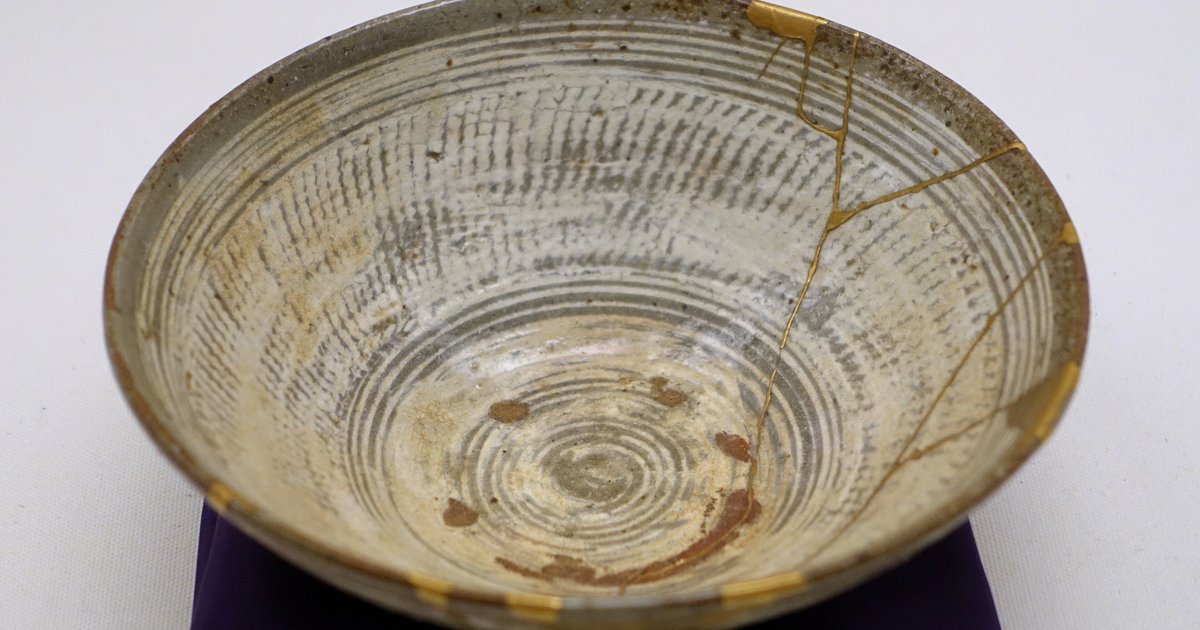 Tigela de cerâmica coreana do século 16, com rachaduras reparadas com laca dourada, sobre fundo cinza claro.
