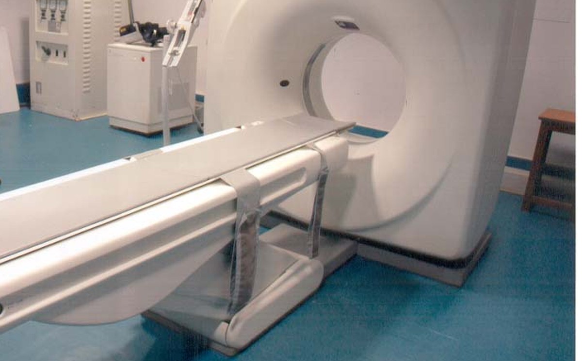 Tomógrafo em sala de exame vazia, com a mesa do paciente em primeiro plano