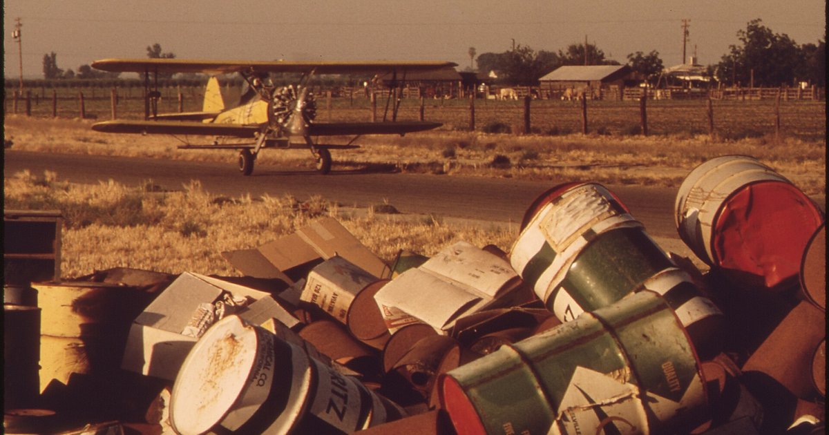 Latas de pesticida descartadas e amontoadas no chão de uma área rural