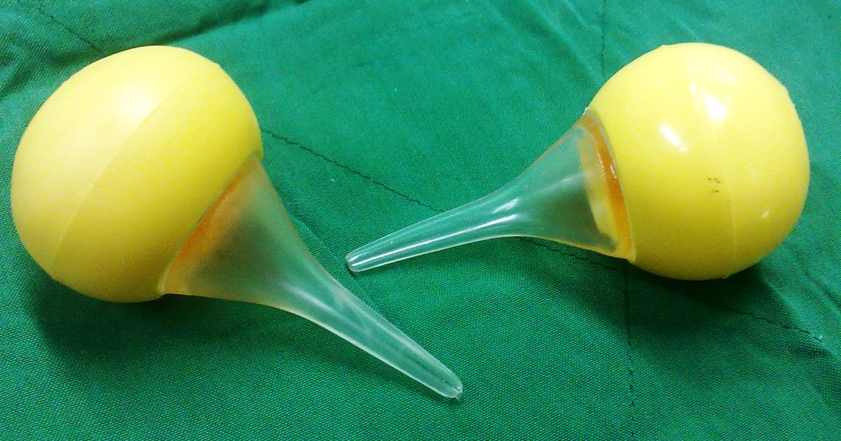 Duas peras de aspiração nasal infantil, de borracha amarela com bico transparente, sobre um campo cirúrgico verde