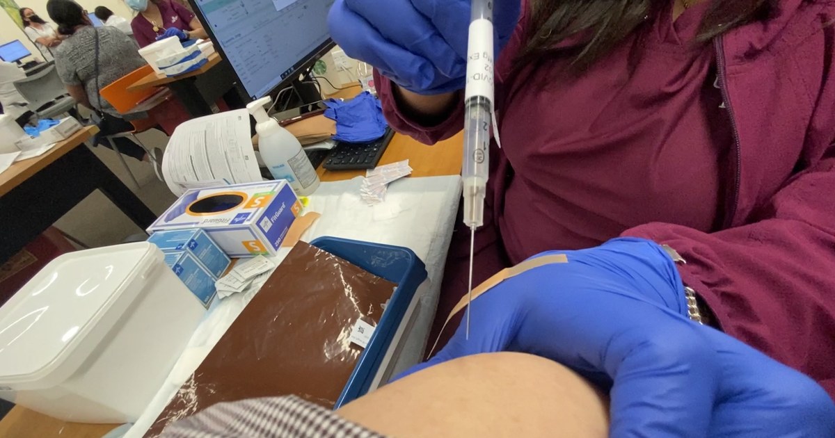 Manos con guantes aplicando una vacuna intramuscular en el brazo en un puesto de vacunación