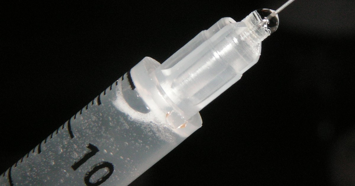 Spritze mit feiner Nadel, bereit zur Injektion, vor dunklem Hintergrund