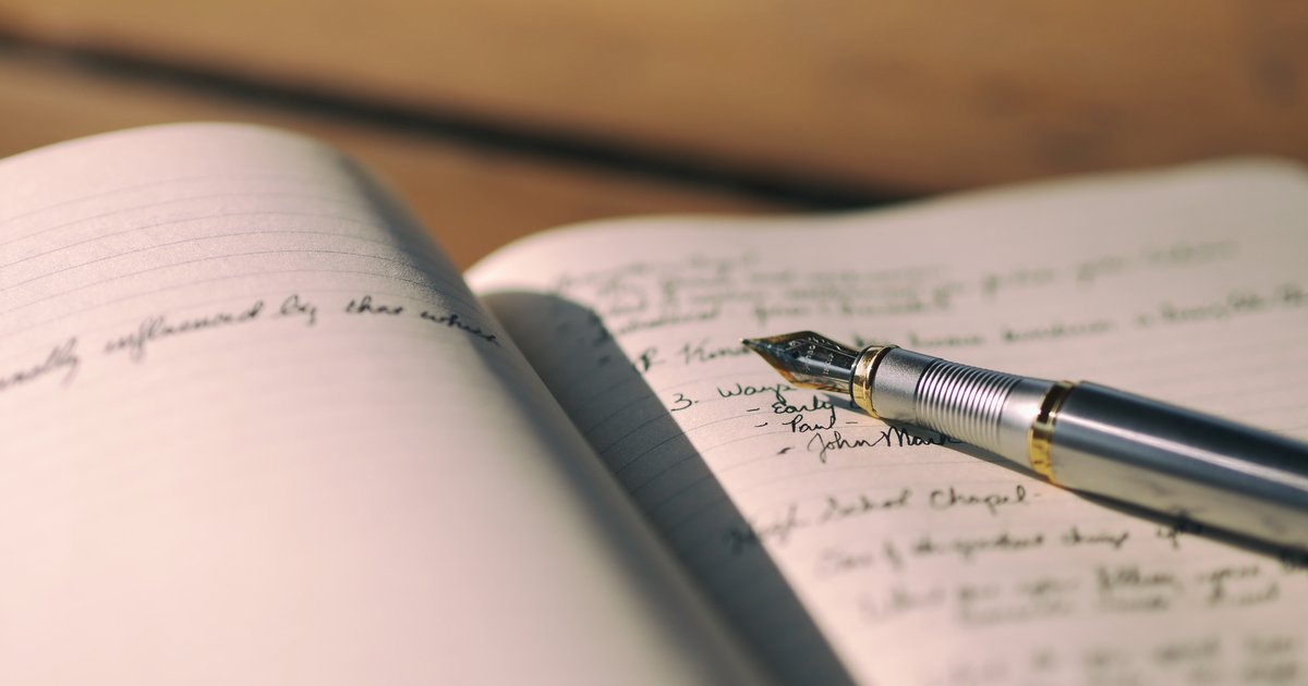 Caneta-tinteiro preta sobre caderno aberto com linhas manuscritas, vista aproximada