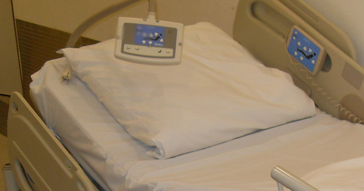 Cabeceira de um leito hospitalar vazio com travesseiro branco e controle de posição apoiado sobre ele