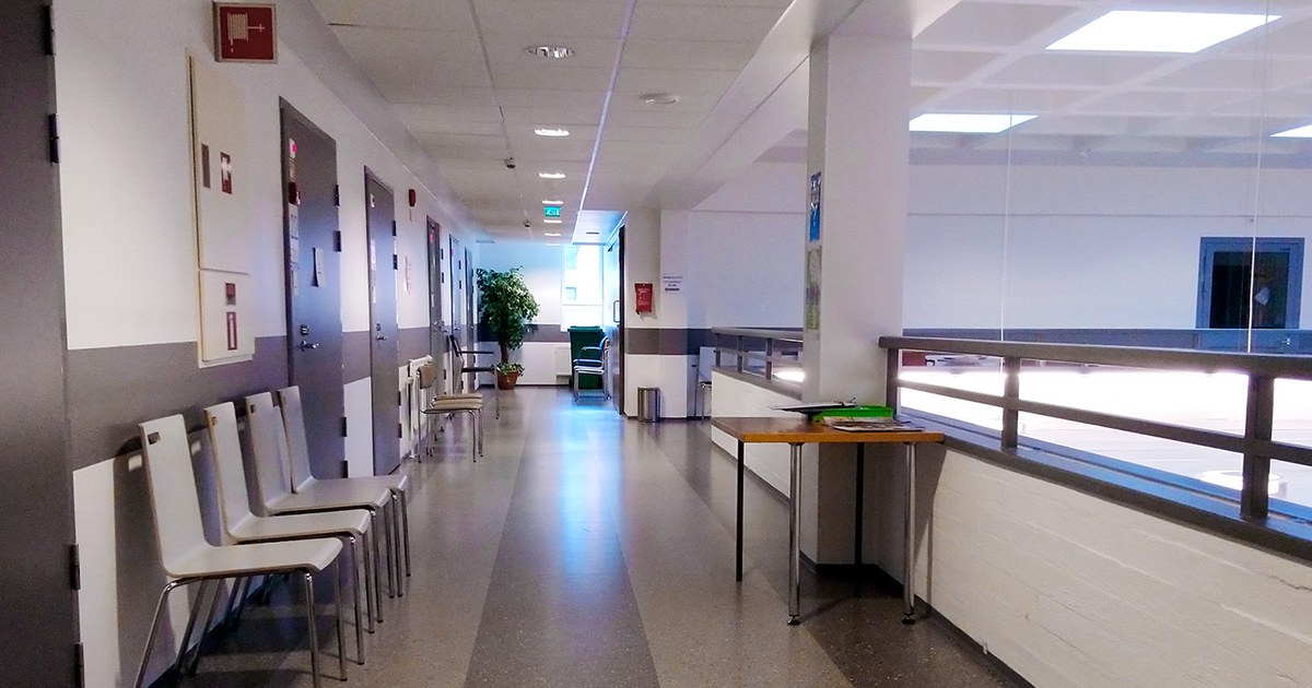 Corredor vazio de um centro de saúde com cadeiras brancas encostadas na parede e piso claro