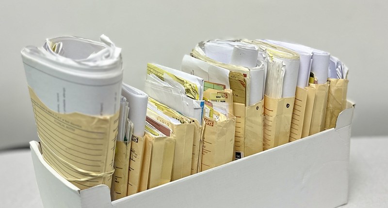 Caixa branca com envelopes de prontuário médico em papel pardo, enrolados e enfileirados