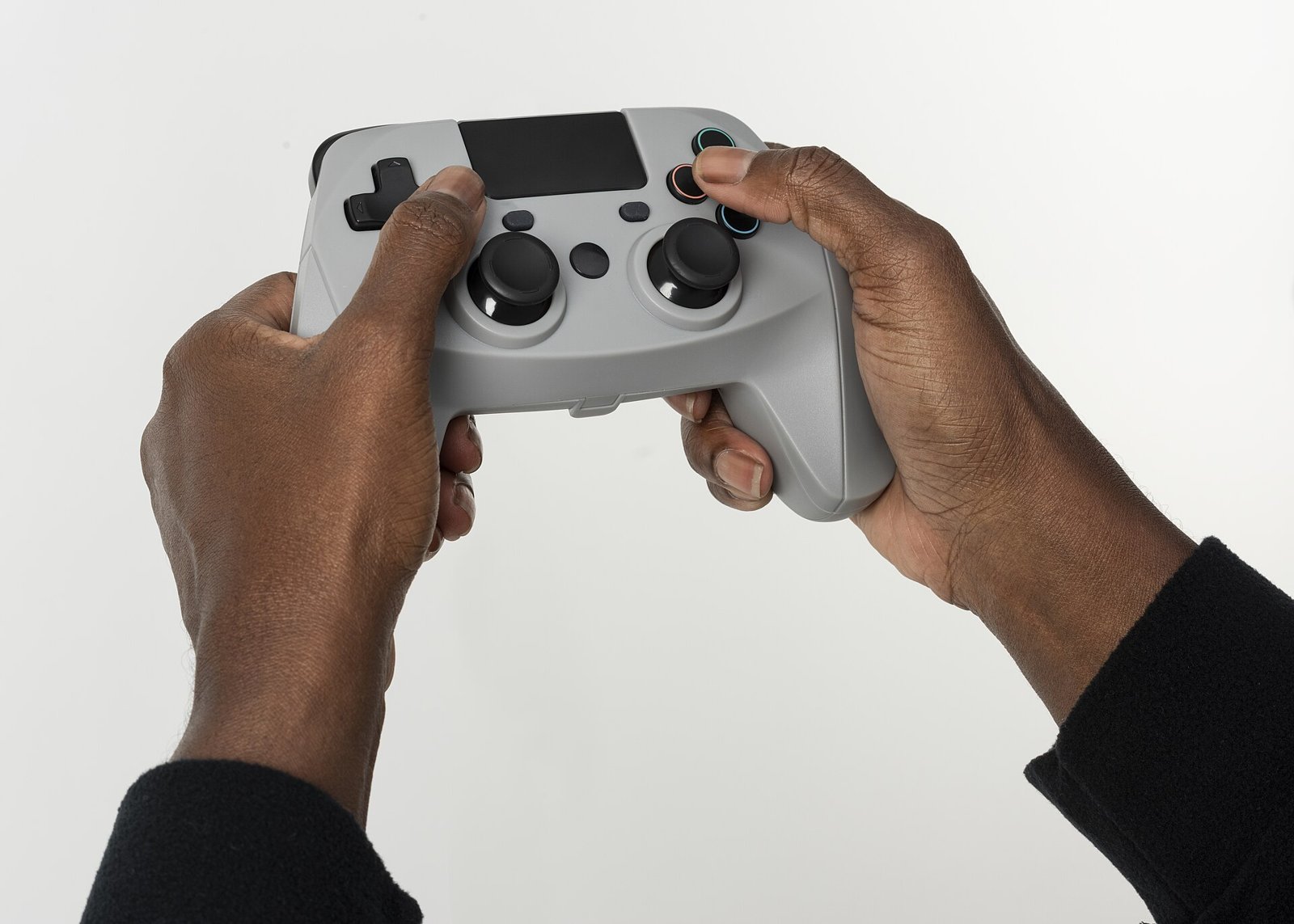 Two hands holding a light gray video game controller, with the thumbs on the buttons, against a white background.