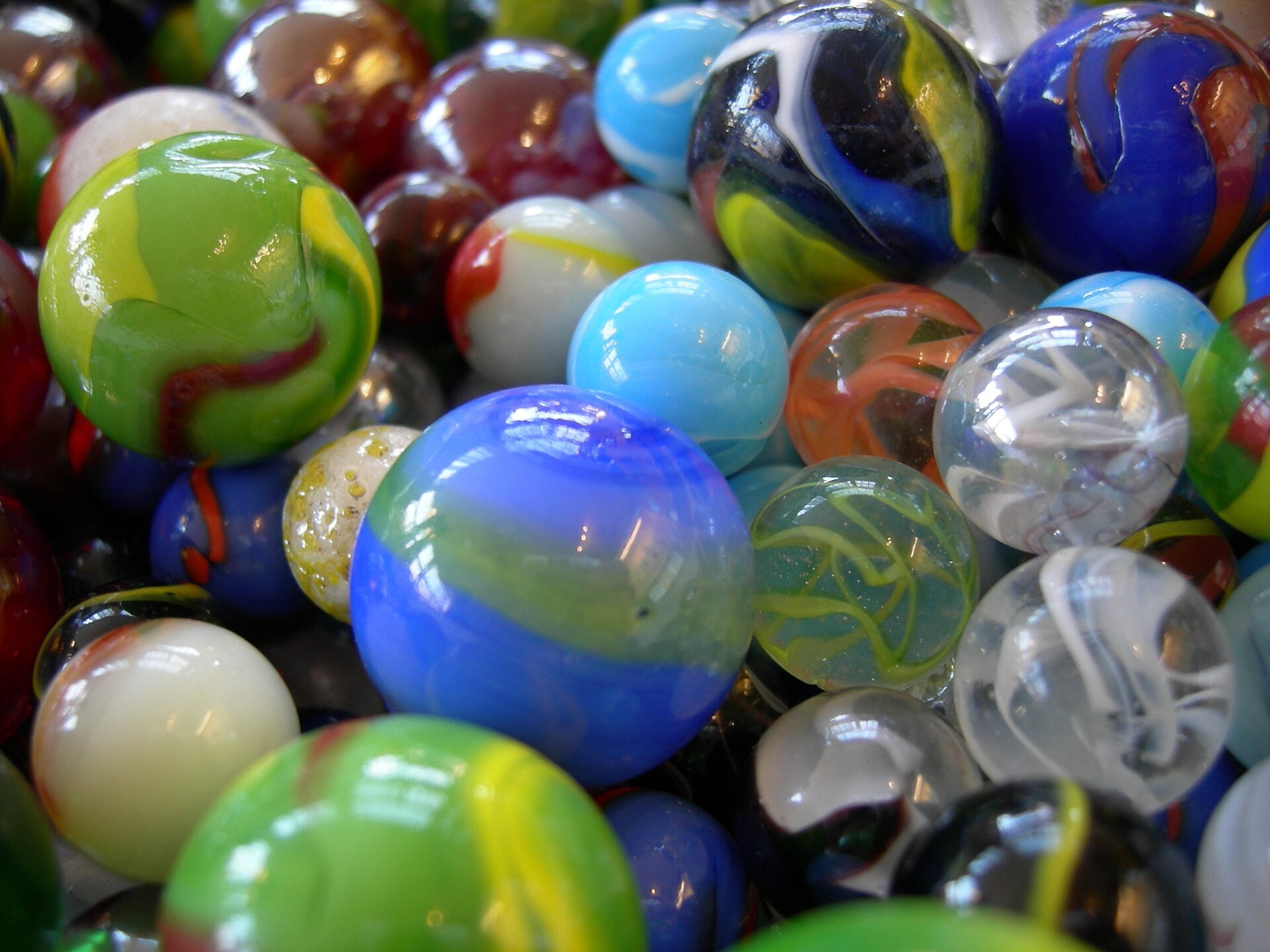 Close-up of dozens of colorful marbles piled up, with green, blue, yellow, red and white spirals inside the glass, some transparent and others milky.
