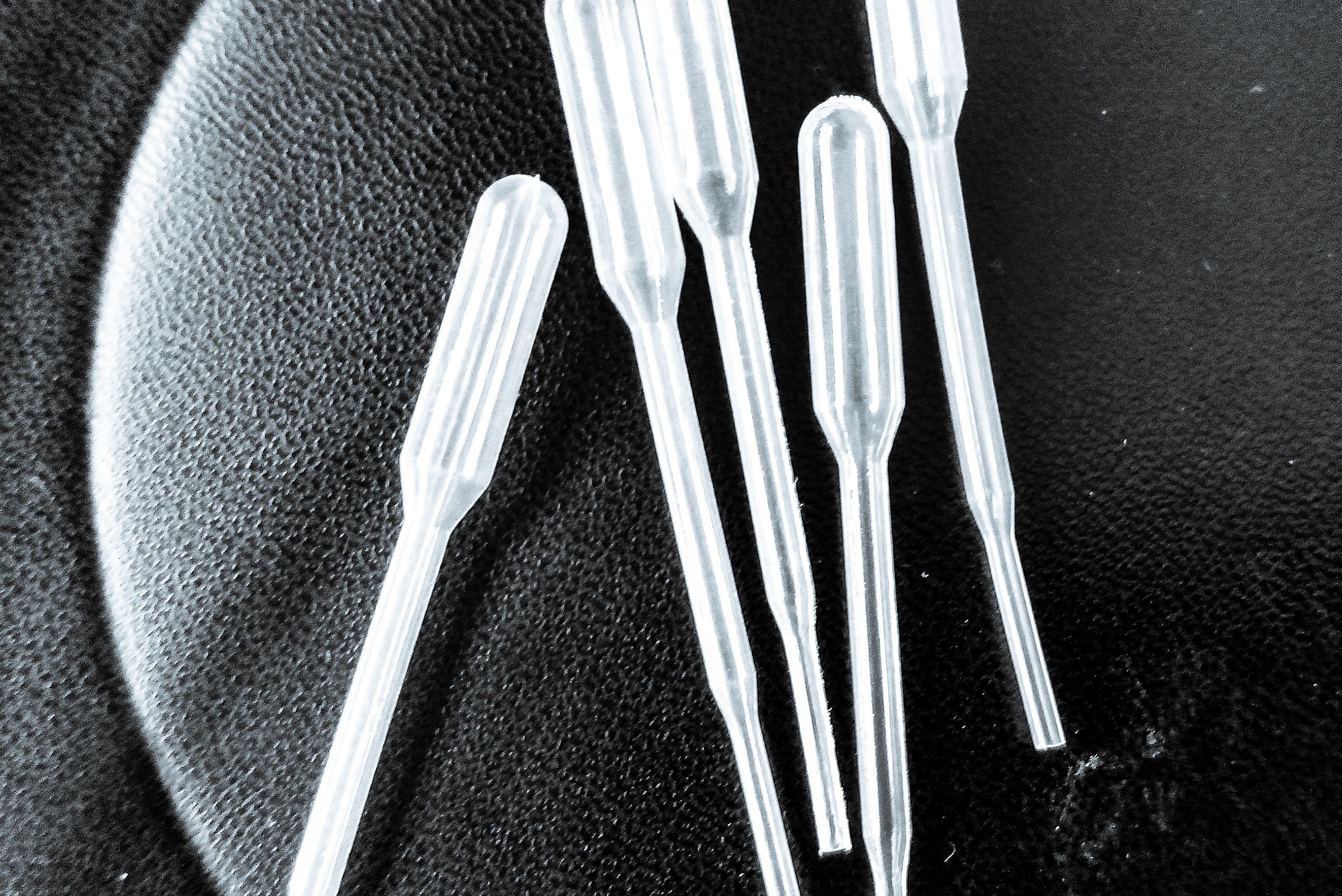 Cinco pipetas plásticas transparentes de laboratório sobre uma superfície escura