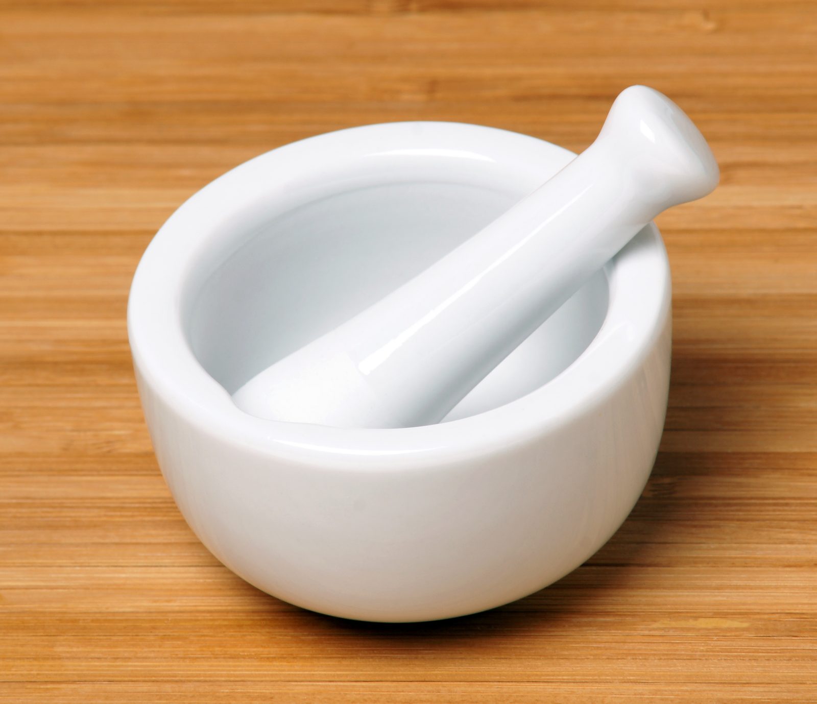 Pilão e almofariz de porcelana branca sobre uma superfície de madeira clara.