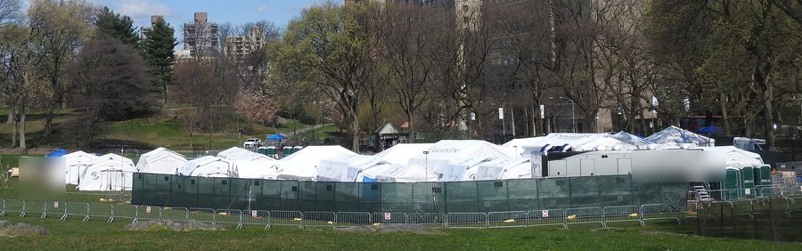 Hospital de campanha em tendas brancas montado num gramado, cercado por grades
