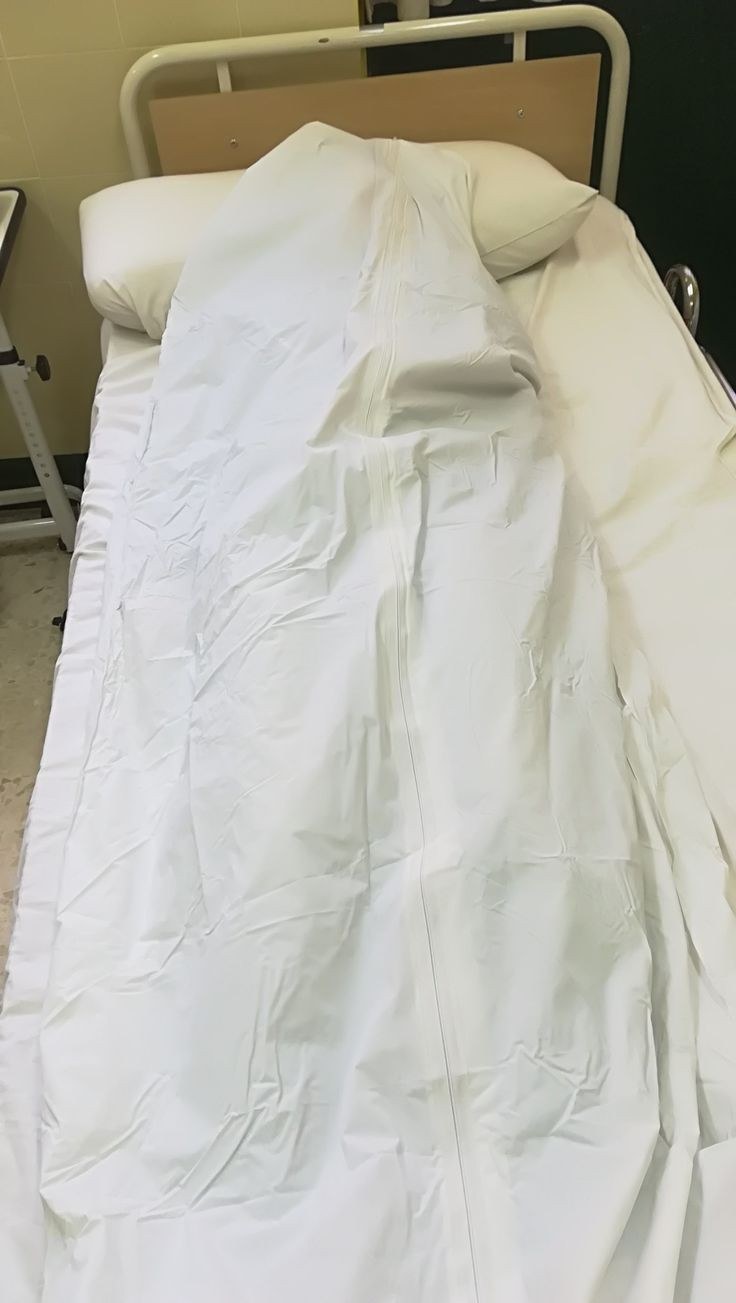 Leito hospitalar vazio com lençóis brancos, junto a uma parede clara