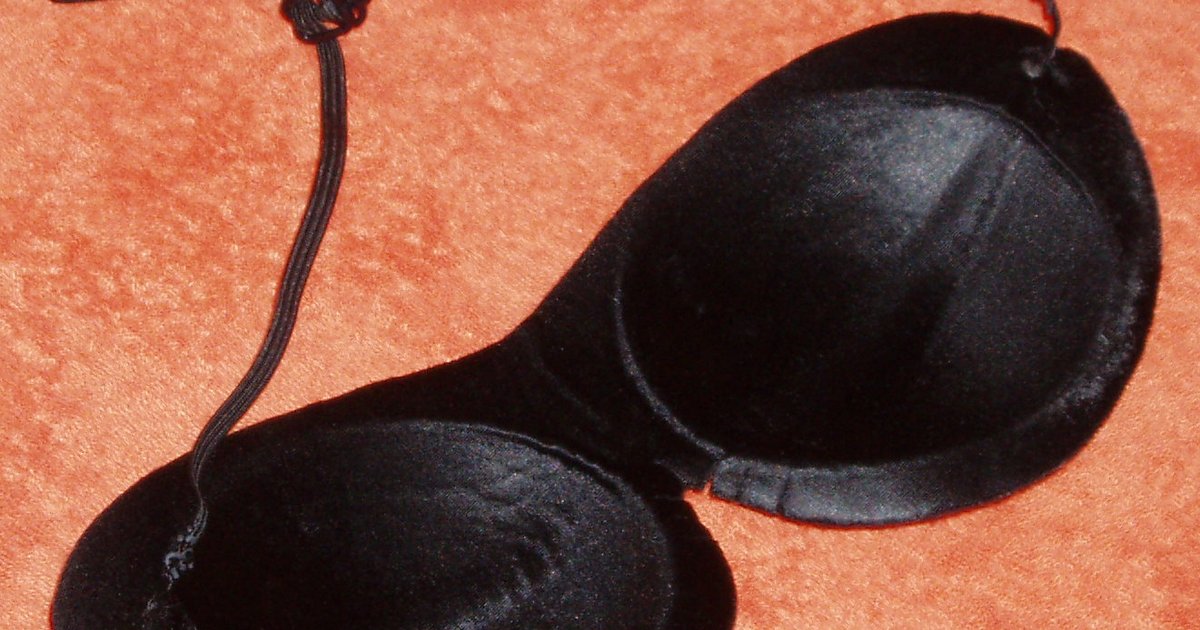 Máscara de dormir preta de tecido acetinado com elástico sobre fundo laranja texturizado