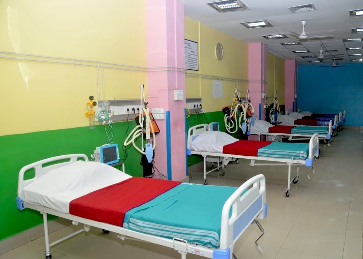 Enfermaria vazia com fileira de leitos hospitalares arrumados e suportes de soro