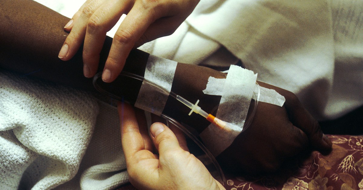 Mãos fixando um acesso venoso no antebraço de paciente para infusão