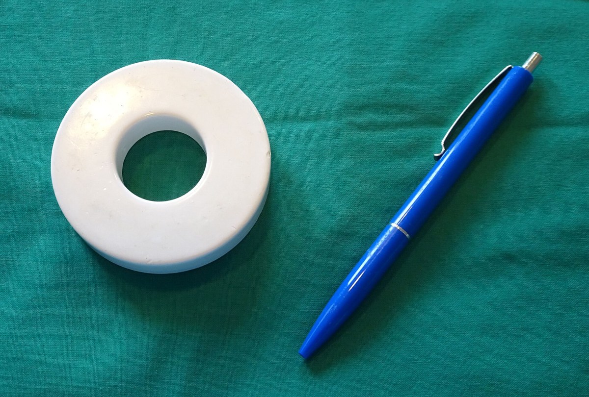 Ímã branco em forma de anel ao lado de uma caneta azul, sobre um tecido verde