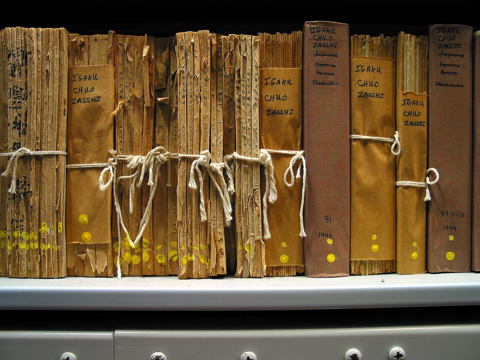 Étagère de bibliothèque avec des volumes anciens reliés d'une revue médicale japonaise, aux dos usés et attachés avec de la ficelle.