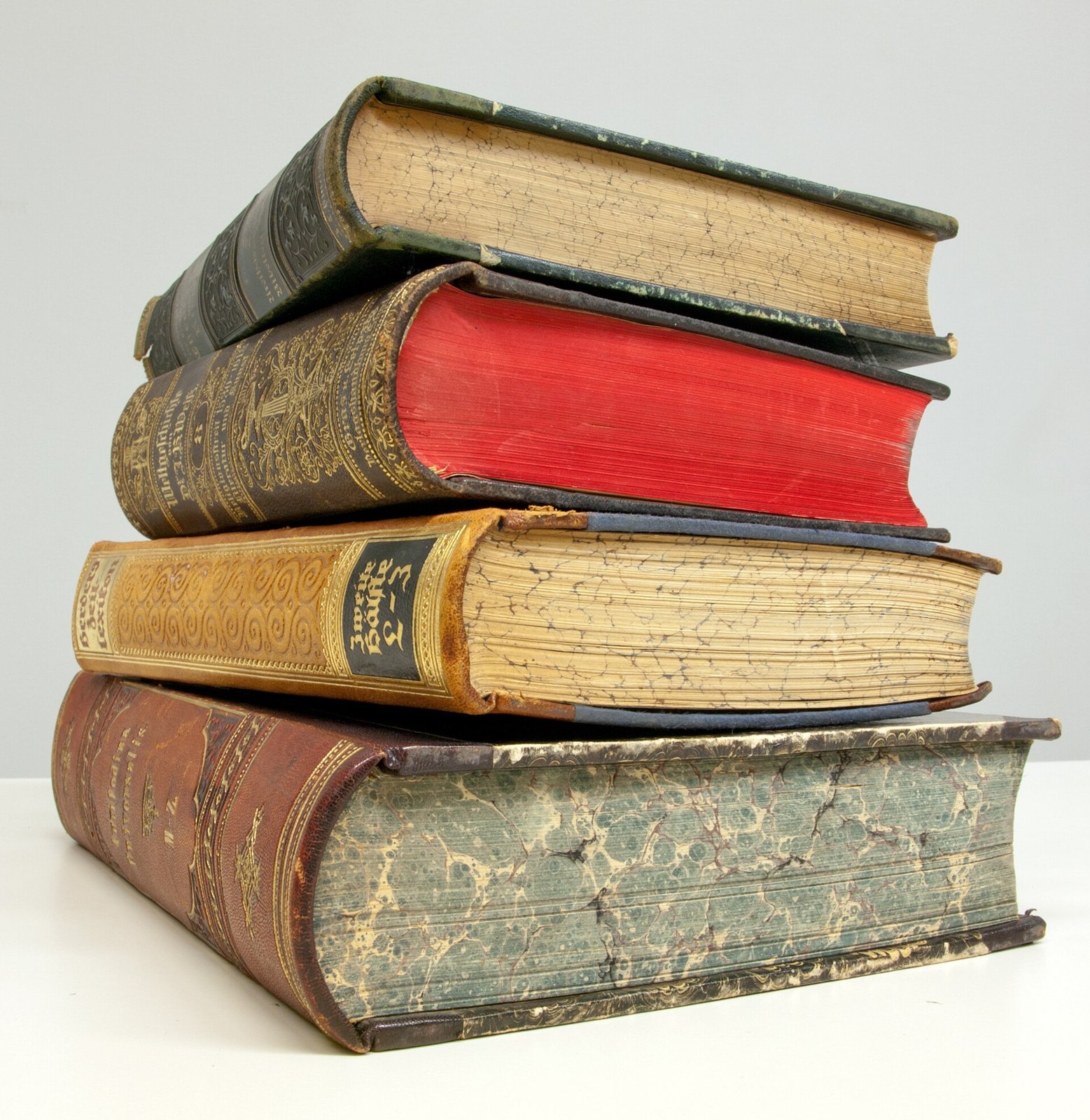 Pile de quatre livres anciens aux dos de cuir décorés de dorures, l'un d'eux avec la tranche des pages en rouge et un autre avec la tranche marbrée.