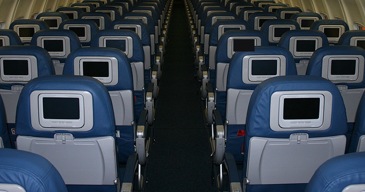 Fileiras de poltronas azuis vazias na cabine de um avião, vistas pelo corredor central