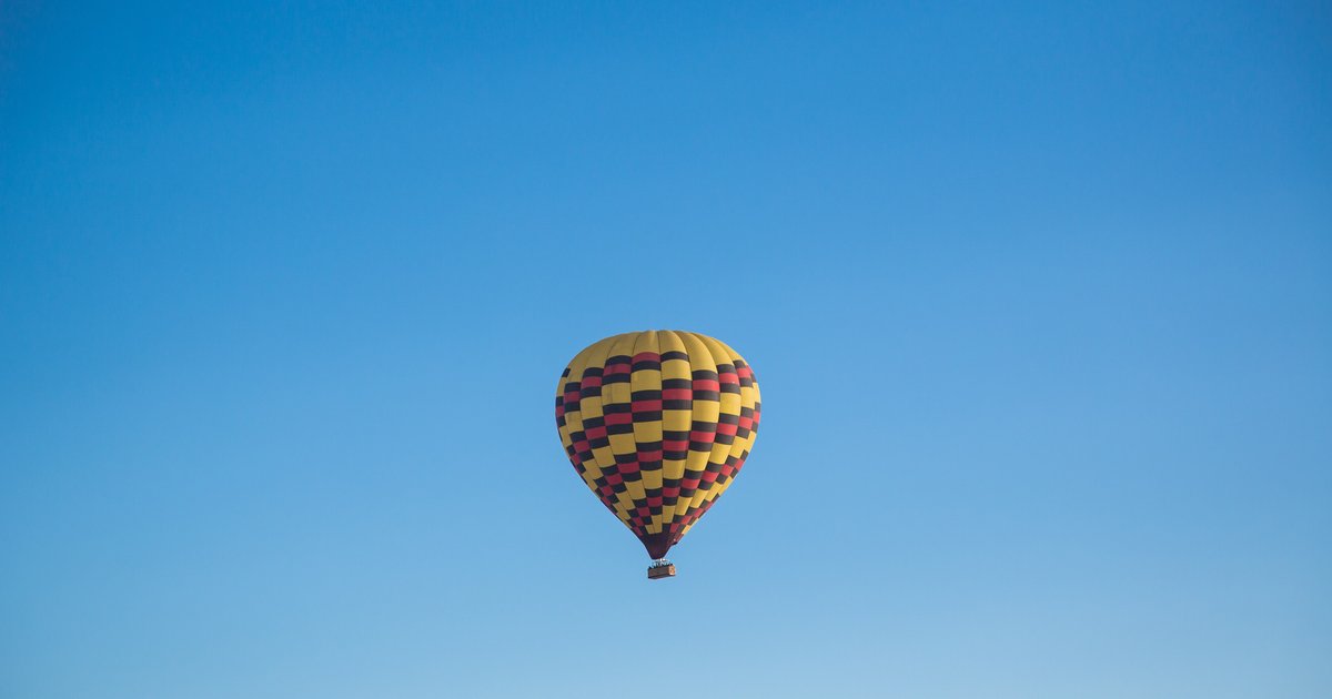 Balão de ar quente com listras amarelas e roxas flutuando sozinho num céu azul limpo, em Napa Valley.