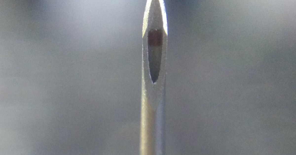 Ponta de uma agulha hipodérmica de metal em close, com fundo cinza desfocado