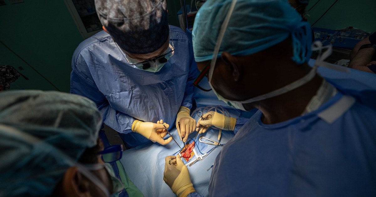 Cirujanos con gorro y bata operando el abdomen de un paciente