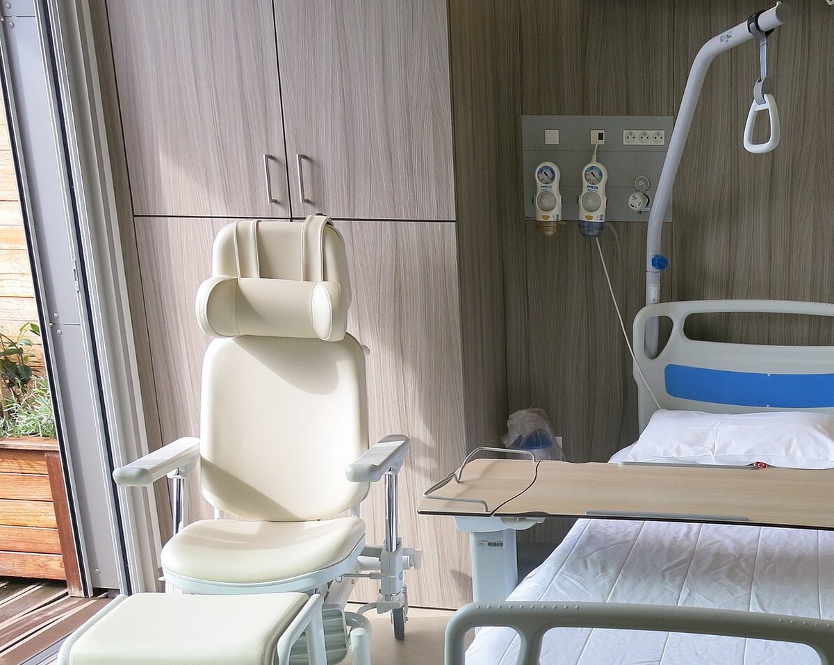 Quarto de internação vazio, com poltrona reclinável clara, cabeceira do leito e painel de gases na parede