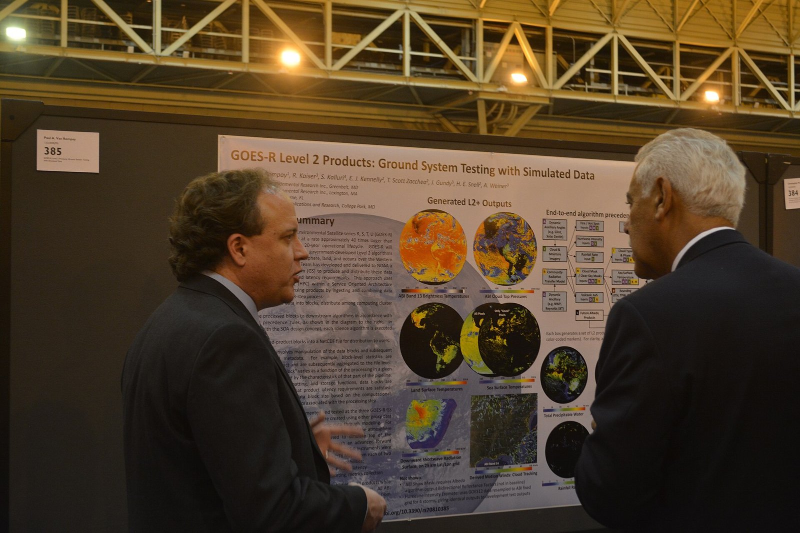 Zwei Männer im Anzug unterhalten sich vor einem wissenschaftlichen Poster mit Grafiken und Satellitenbildern in einem Kongresssaal.