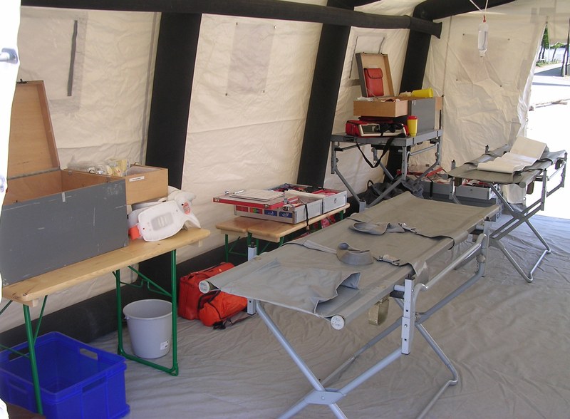 Interior de uma tenda médica de campanha com macas dobráveis, mesa com material e caixas de equipamento