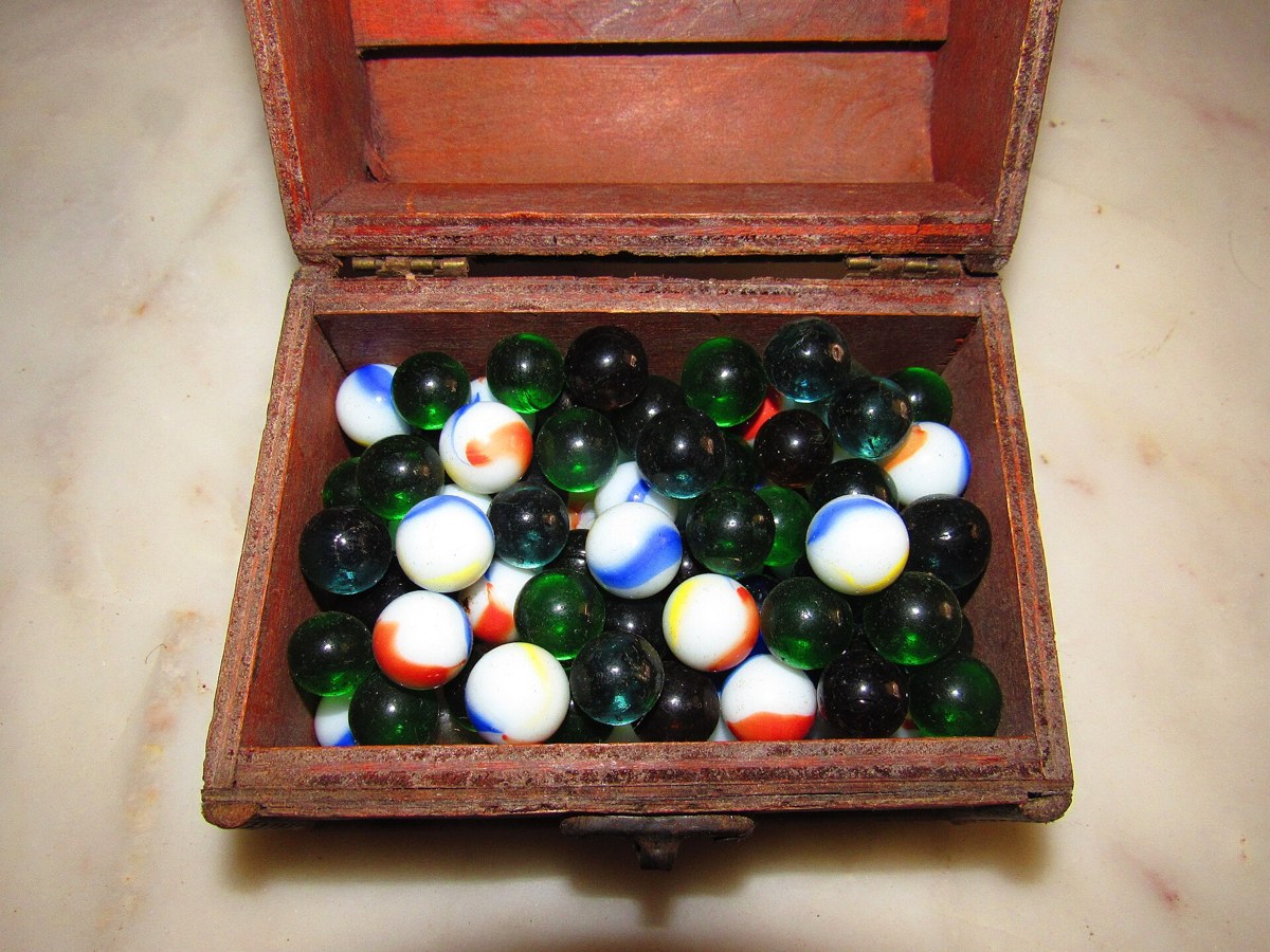 Caixa de madeira com bolinhas de gude coloridas em compartimentos, algumas cheias e outras quase vazias