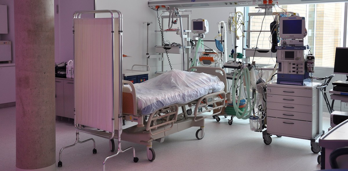 Leito vazio de terapia intensiva coberto por plástico, com biombo, monitores e ventilador ao redor