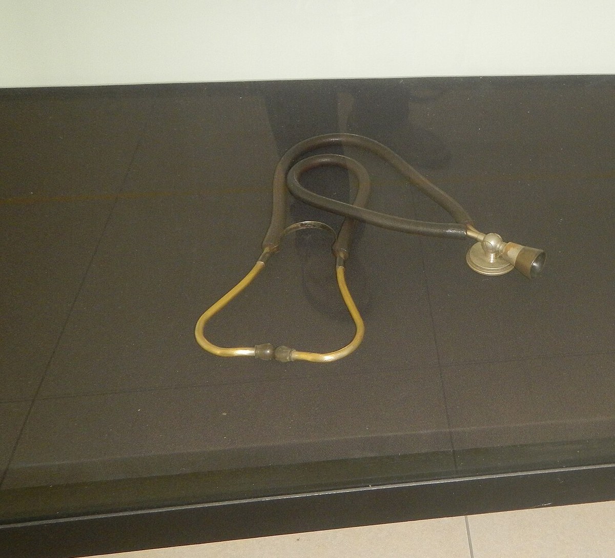 Estetoscópio antigo de tubos escurecidos exposto sobre uma vitrine escura de museu