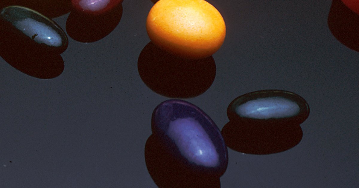 Cápsulas e comprimidos coloridos espalhados sobre fundo escuro com sombras fortes