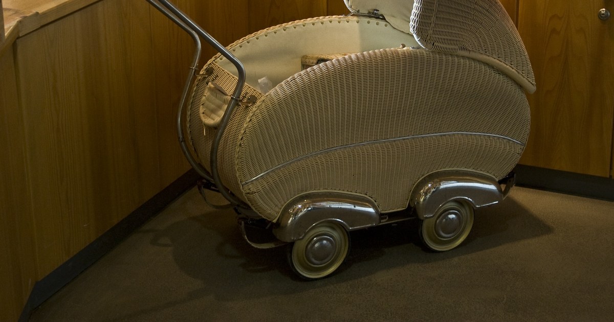 Carrinho de bebê antigo de vime claro com rodas cromadas, em um canto com móveis de madeira