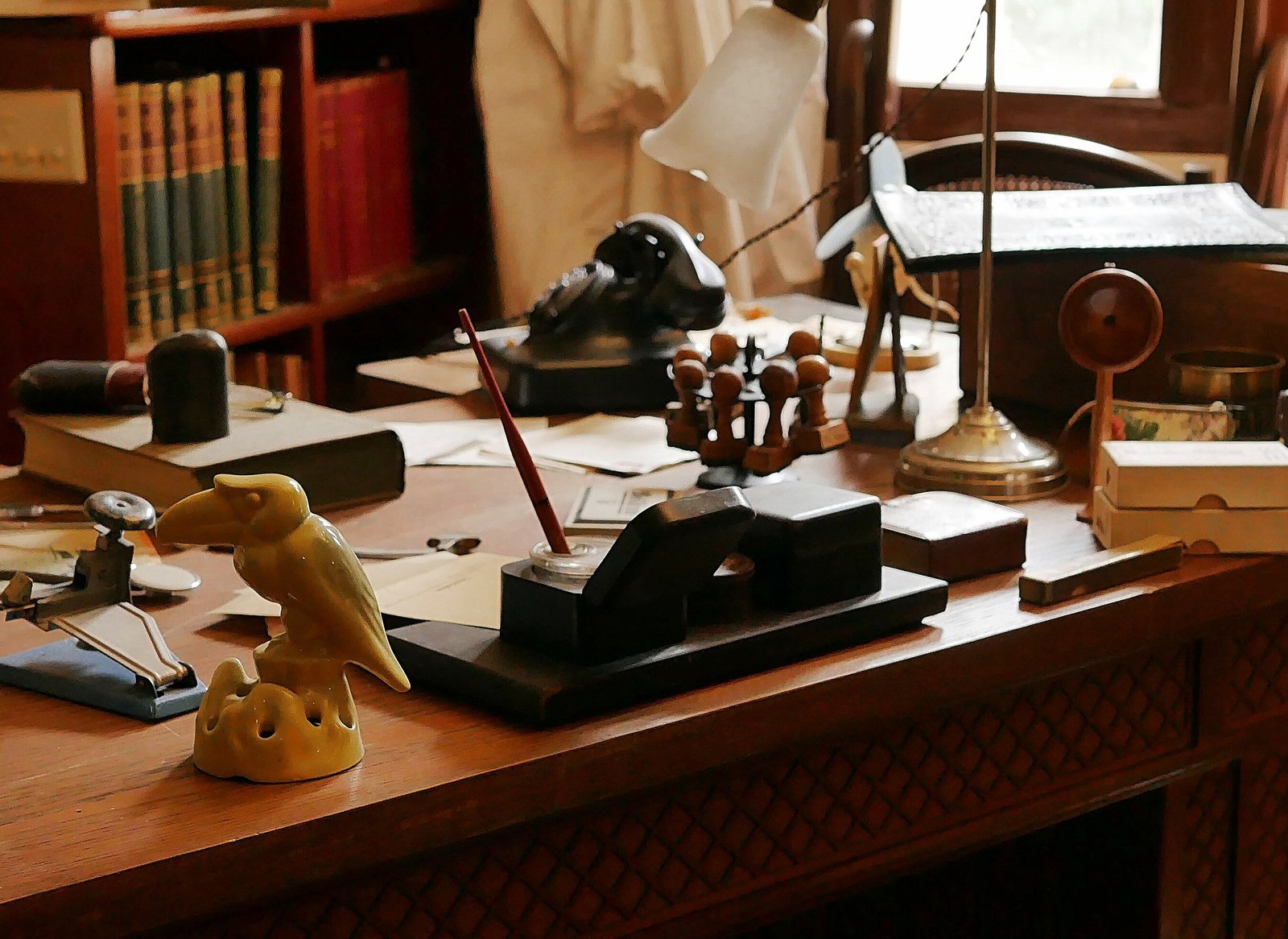 Escrivaninha antiga de consultório médico, com livros, luminária, telefone de disco, carimbos e papéis sobre a mesa de madeira