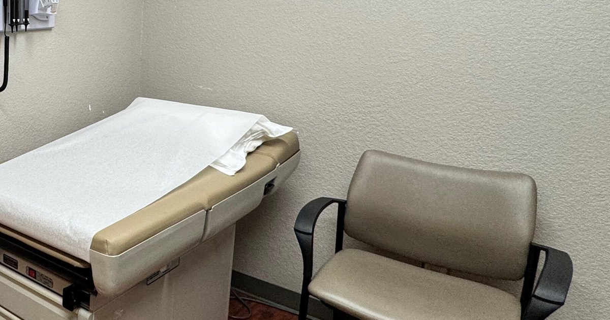 Sala de consulta vazia com maca de exame e cadeira para acompanhante